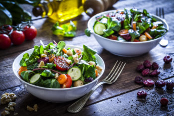 two bowls of salad sitting on wooden table