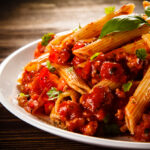 Pasta with meat, tomato sauce and vegetables on white plate | international cuisine in Lone Tree