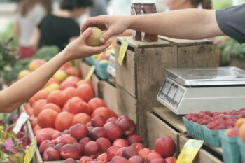 vendor handing a customer an apple at a farmers market | farmers market Lone Tree