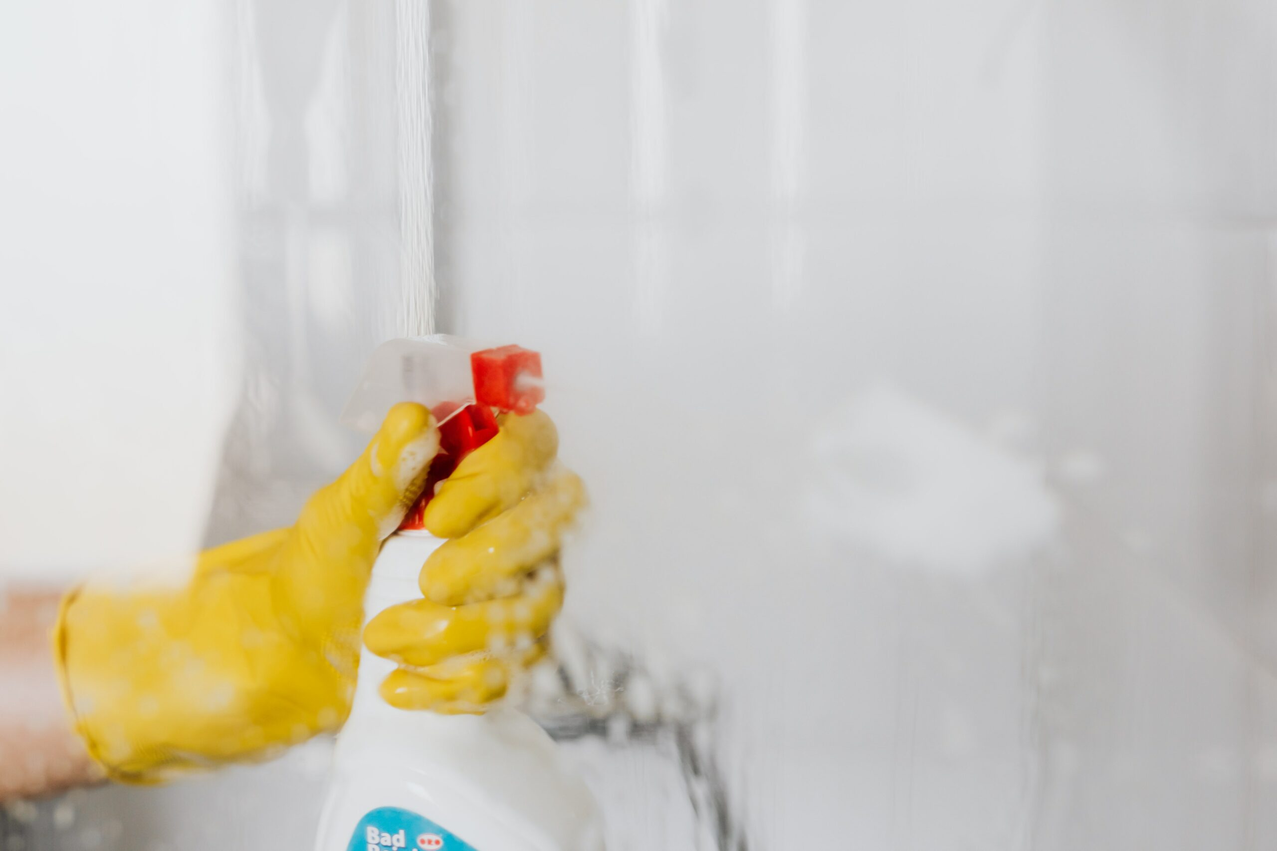 hand with a yellow glove spraying a cleaner in a bathtub | maid services Lone Tree