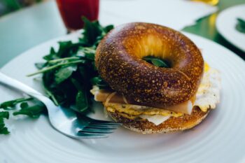 a bagel sandwich with eggs and cheese with spinach and a fork on a white plate | breakfast lone tree