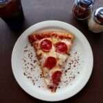 a slice of pizza on a plate with pepper and parmesan cheese with a soda | pizza Lone Tree