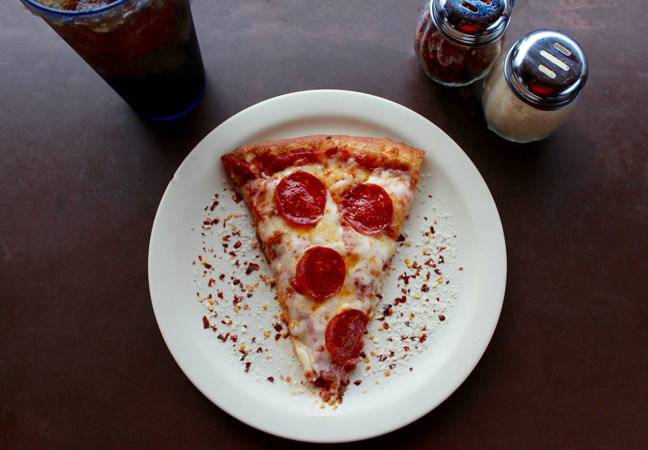 a slice of pizza on a plate with pepper and parmesan cheese with a soda | pizza Lone Tree